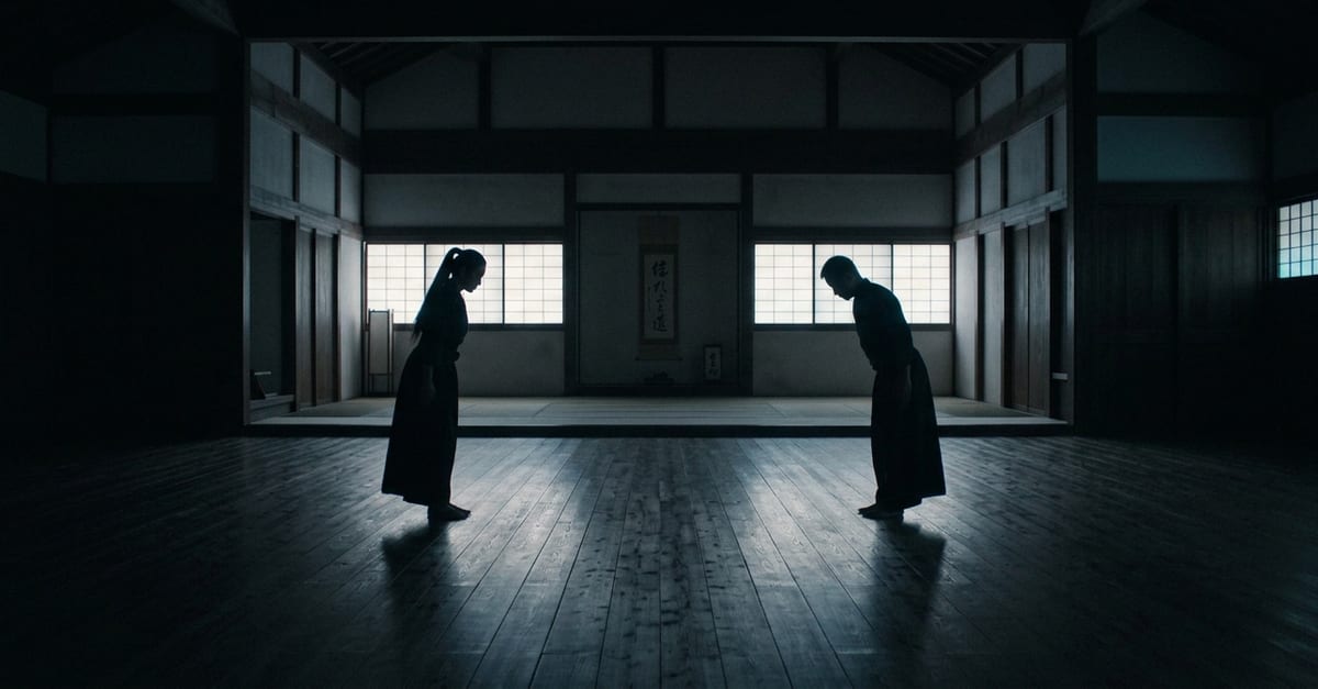 Two figures bowing to each other across a dim dojo at dawn