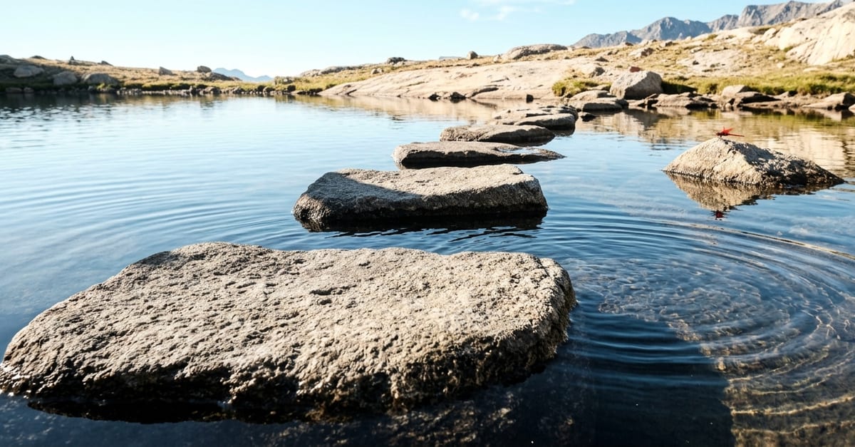 Five stepping stones crossing still water towards a sunlit bank